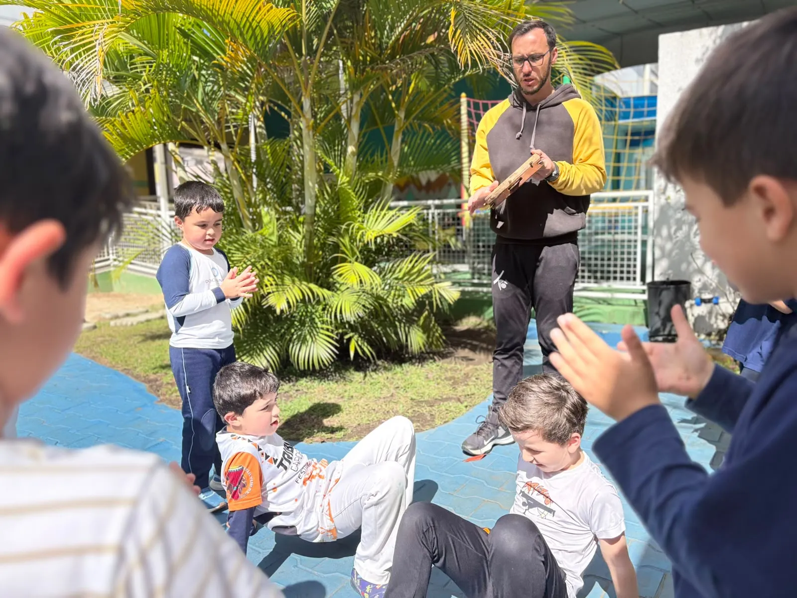 Professor e crianças participando de uma roda de capoeira na área externa