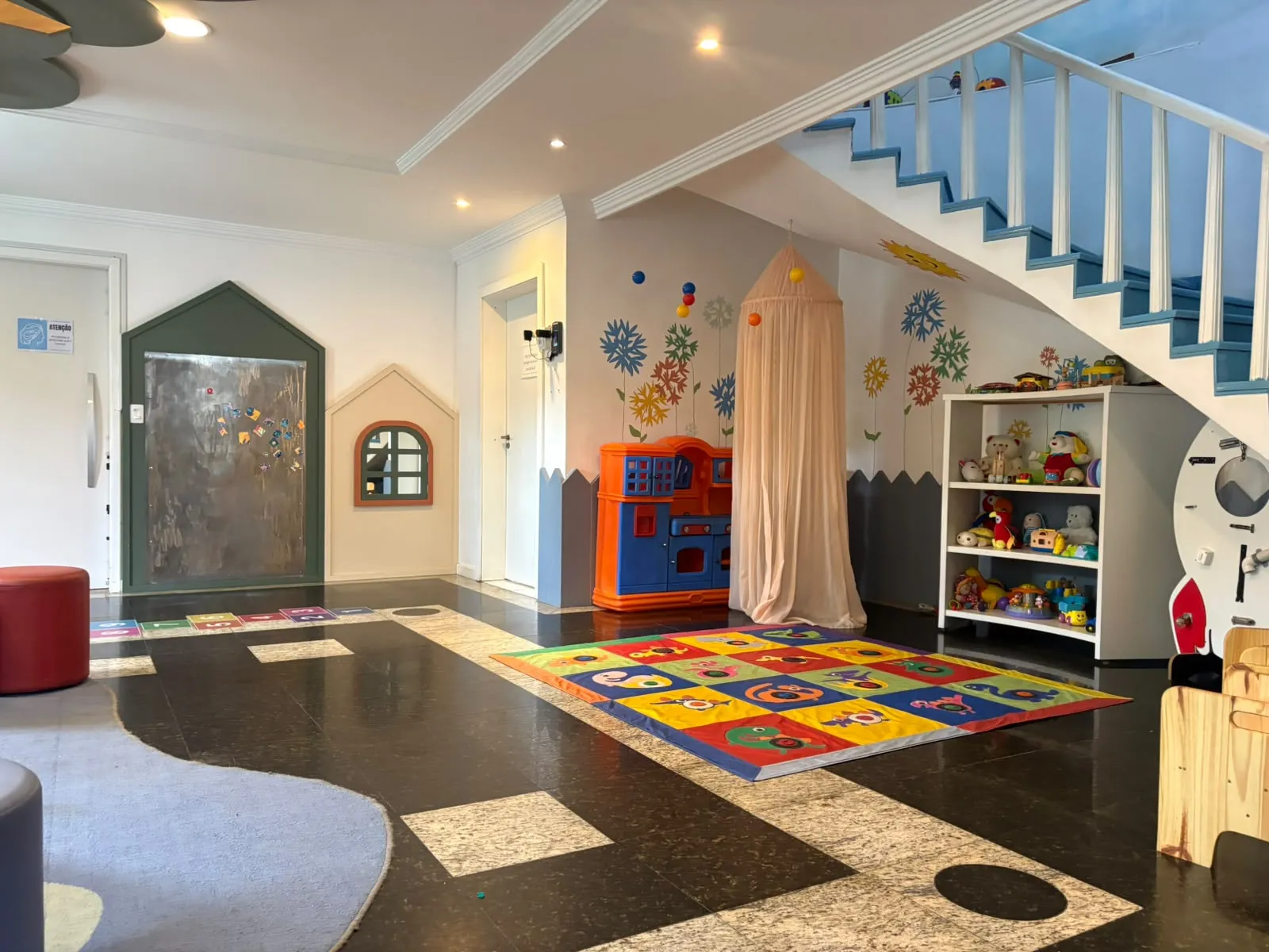 Espaço de brincar interno com casinhas, brinquedos de faz de conta e tapete colorido