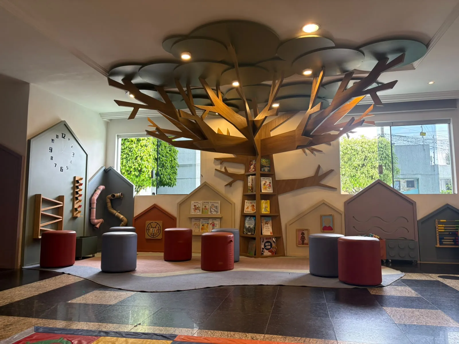 Sala de leitura da Doce Ninho com estante em forma de árvore, livros e bancos para as crianças